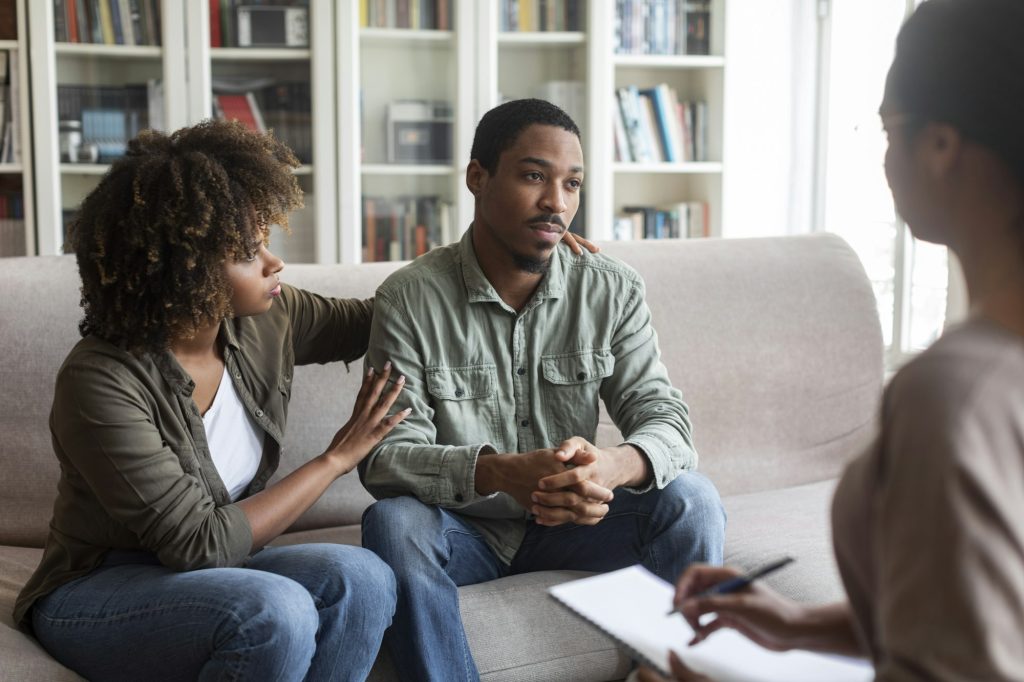 Loving black woman embracing her depressed husband, therapy session