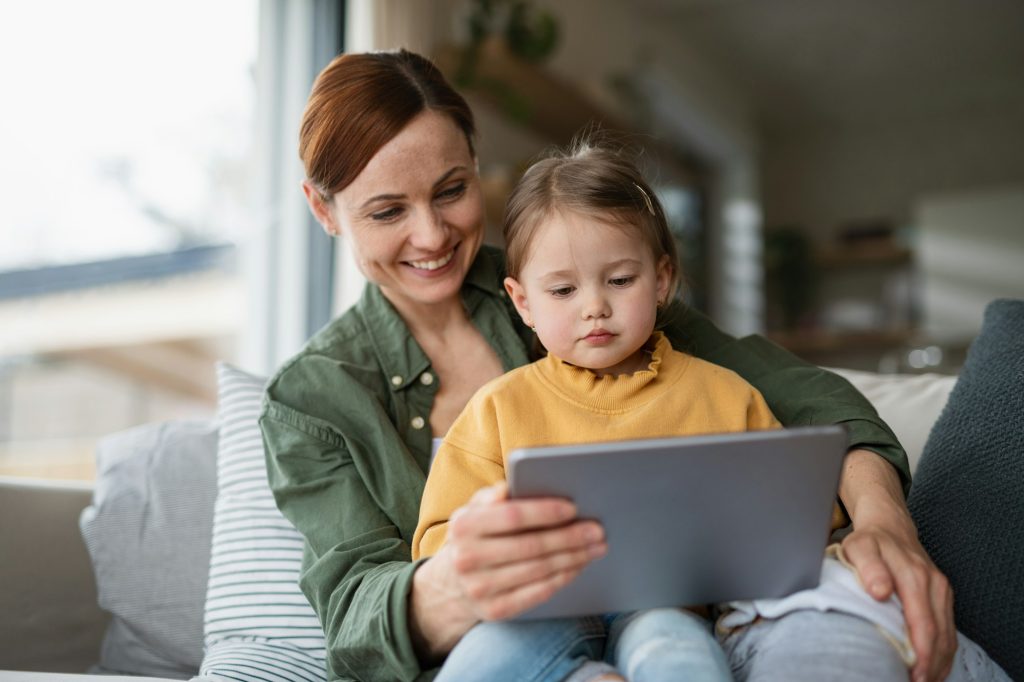 Mother with daughter watching kids programme on tablet indoors at home, single parenting concept.