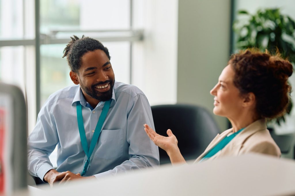 Happy black businessman talking to female colleague while working at corporate office.